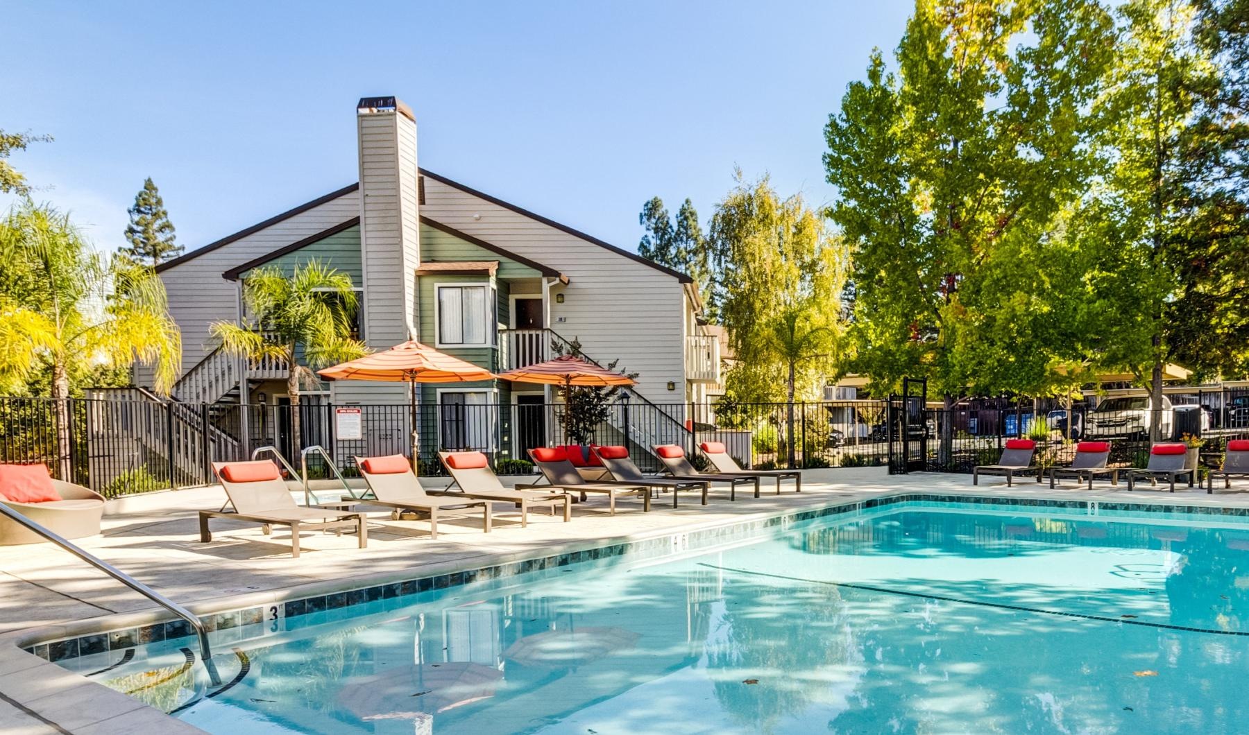 a swimming pool with chairs and umbrellas next to a house